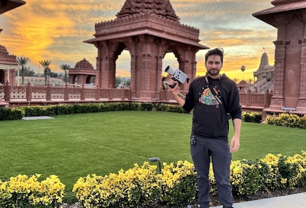 Lukas Valderrama standing outside temple, holding movie camera