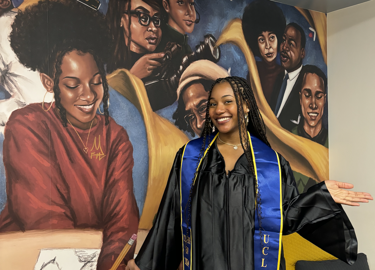 Maia Faith Hadaway posing in front of her mural “A Seat at the Table” in the Black Bruin Resource Center 