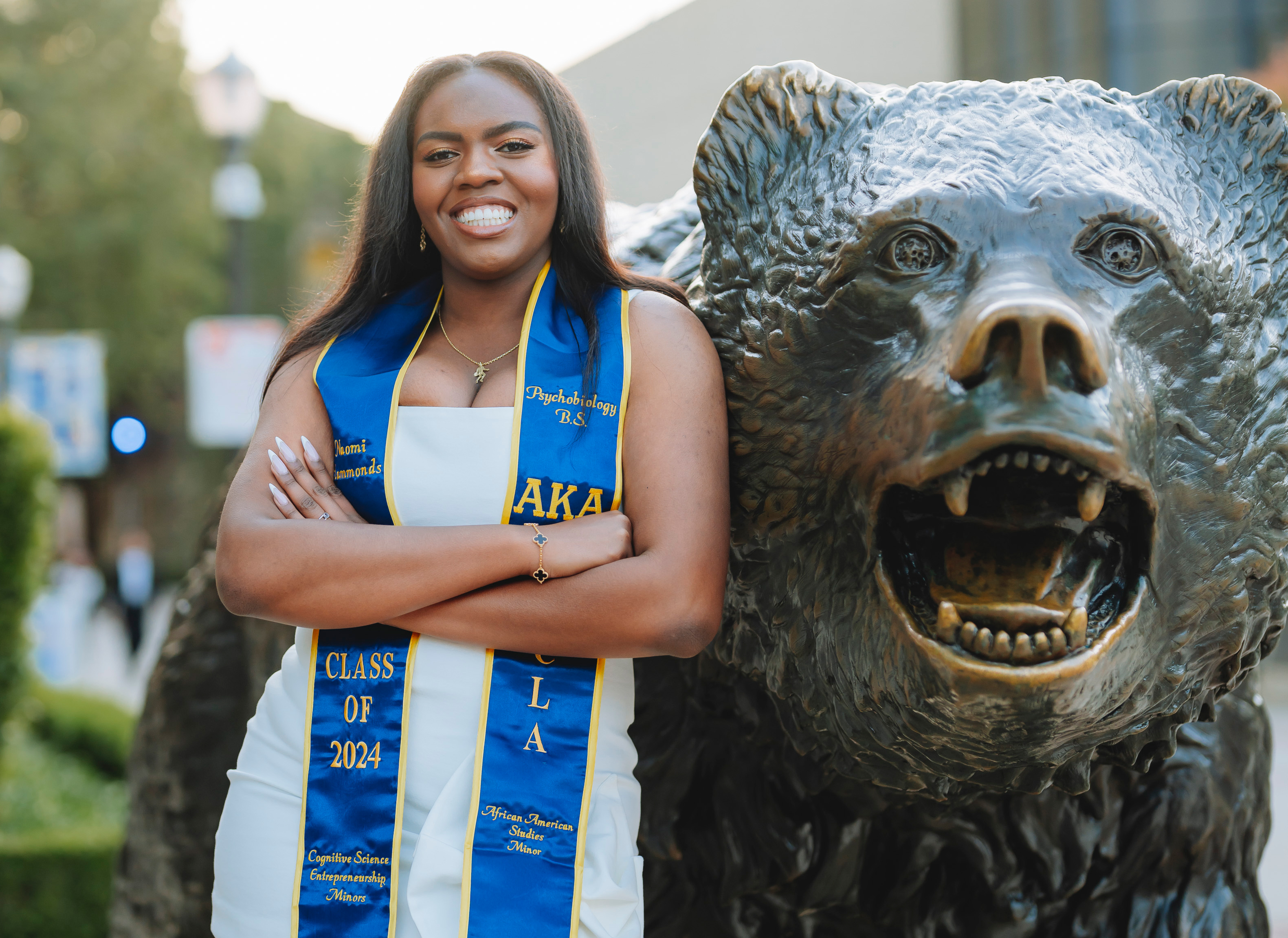 Naomi Hammonds wearing graduation sash, stands next to bear statue
