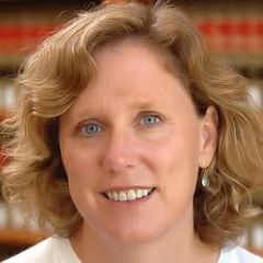 Headshot of Ann Carlson wearing a light colored top and drop earrings.