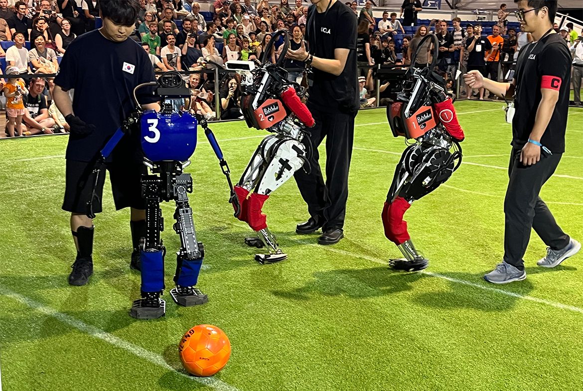 Three students and humanoid robots with a soccer ball