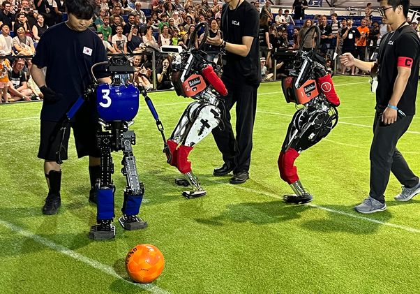Three students and humanoid robots with a soccer ball