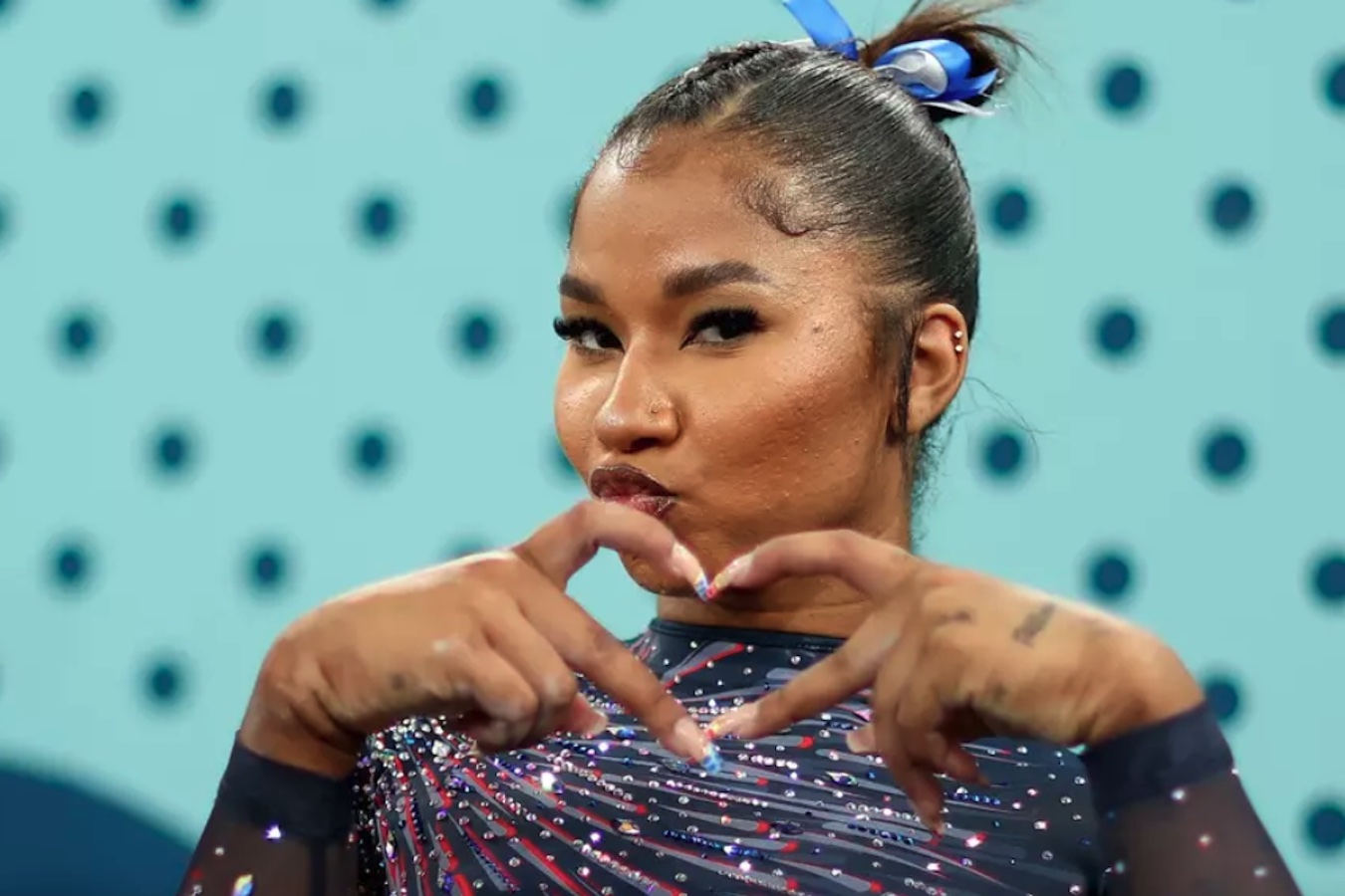 Gymnast Jordan Chiles in a leotard, making a heart sign with her hands