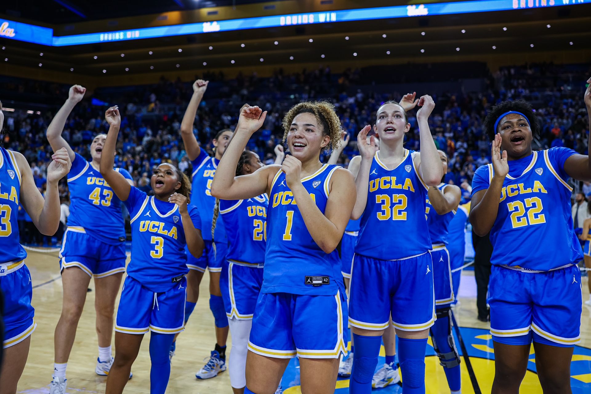 Members of the UCLA Women's Basketball team stand on the court and cheer during a home game. 
