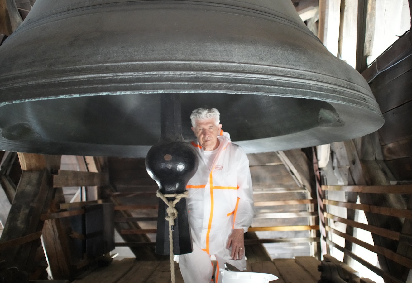 Bill Fontana, holding a construction helmet, stands in front of the Emmanuel bell at Notre Dame in Paris, the oldest of the cathedral’s 10 bells.