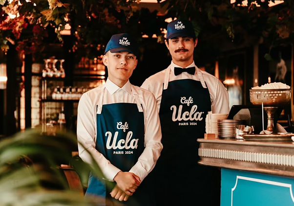Two servers wearing Café UCLA aprons and caps