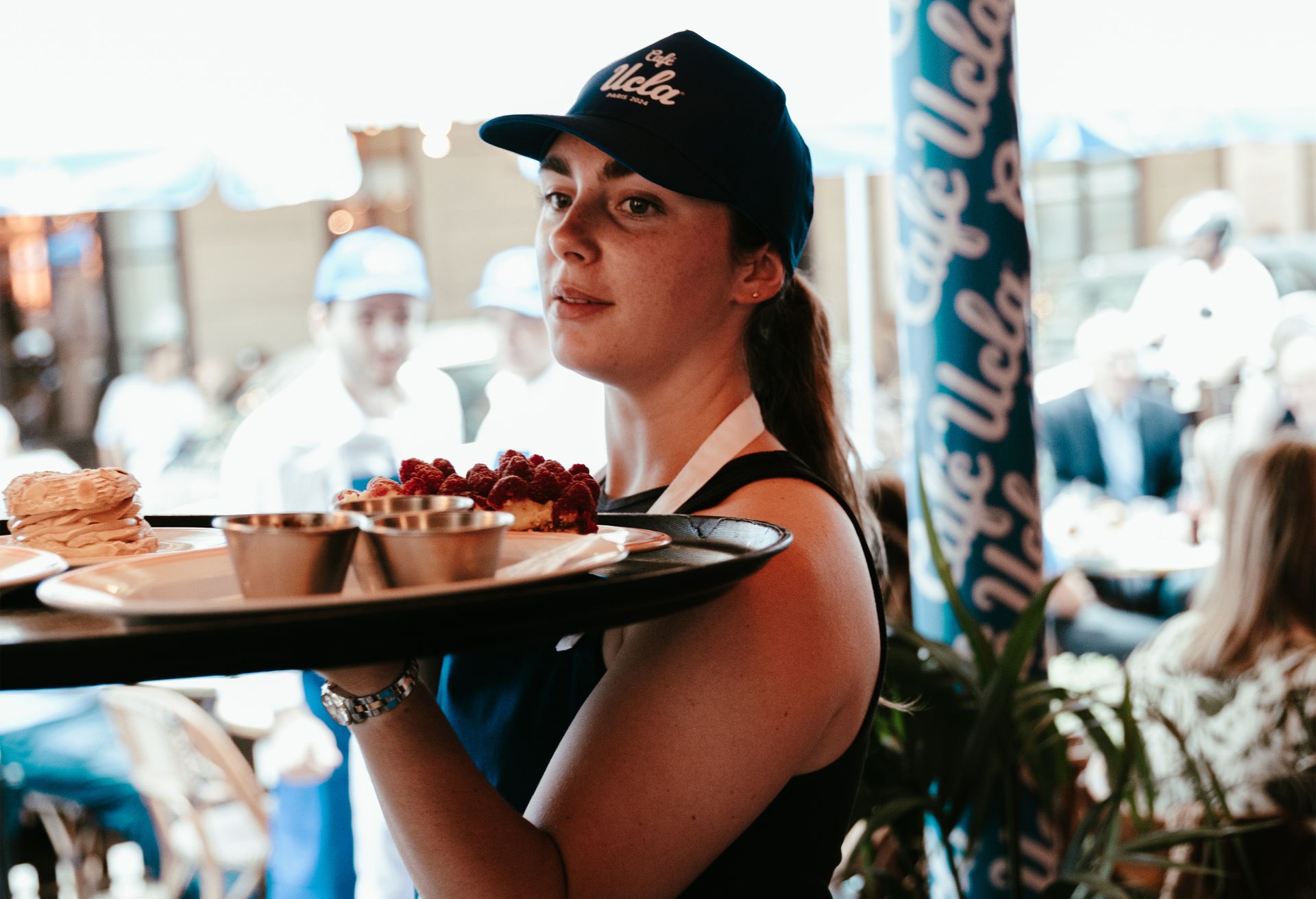 Server with Café UCLA hat carrying plate of food