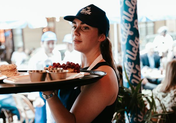 Server with Café UCLA hat carrying plate of food