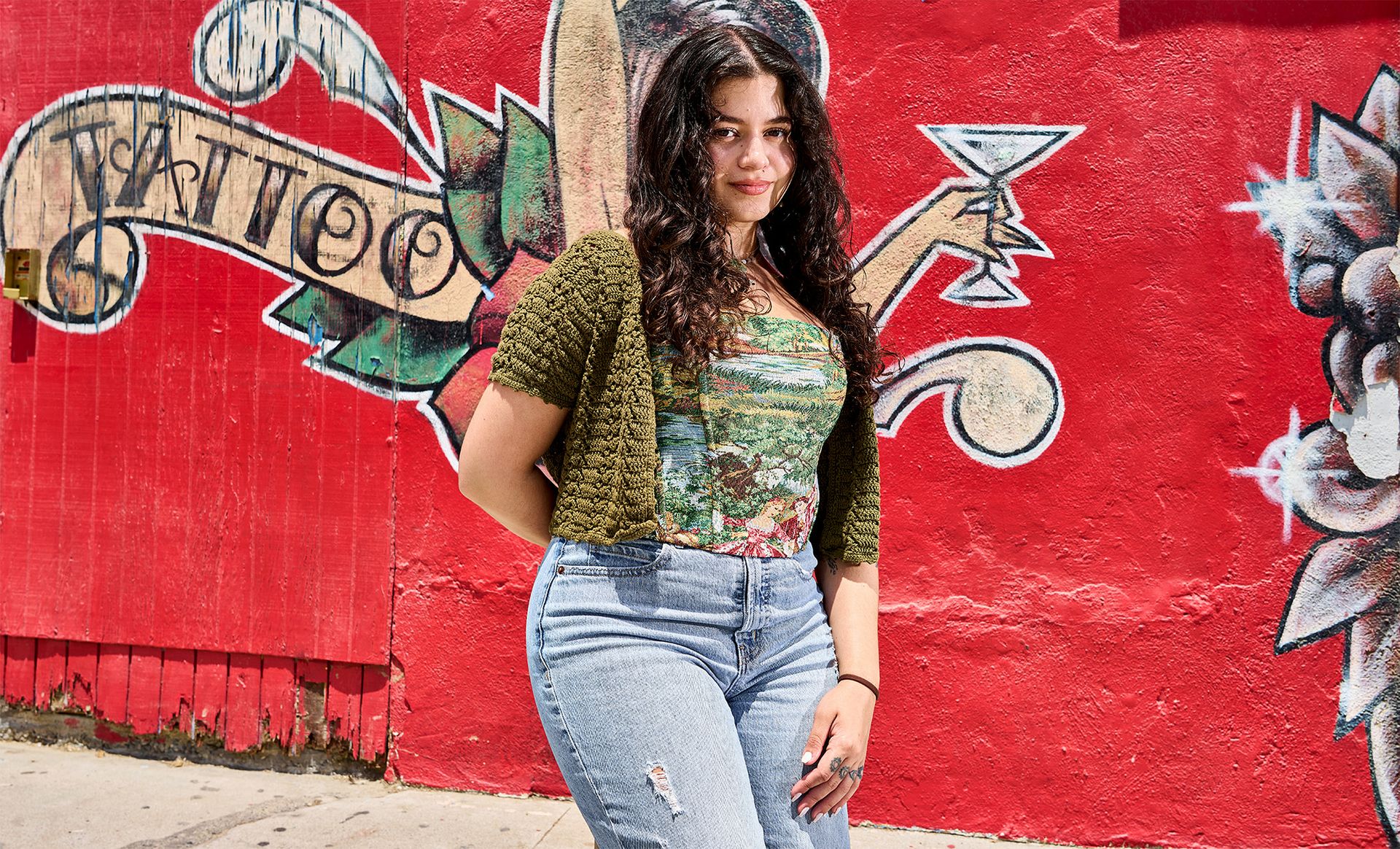 Cristina Williams stands in front of red wall with the word “tattoo”