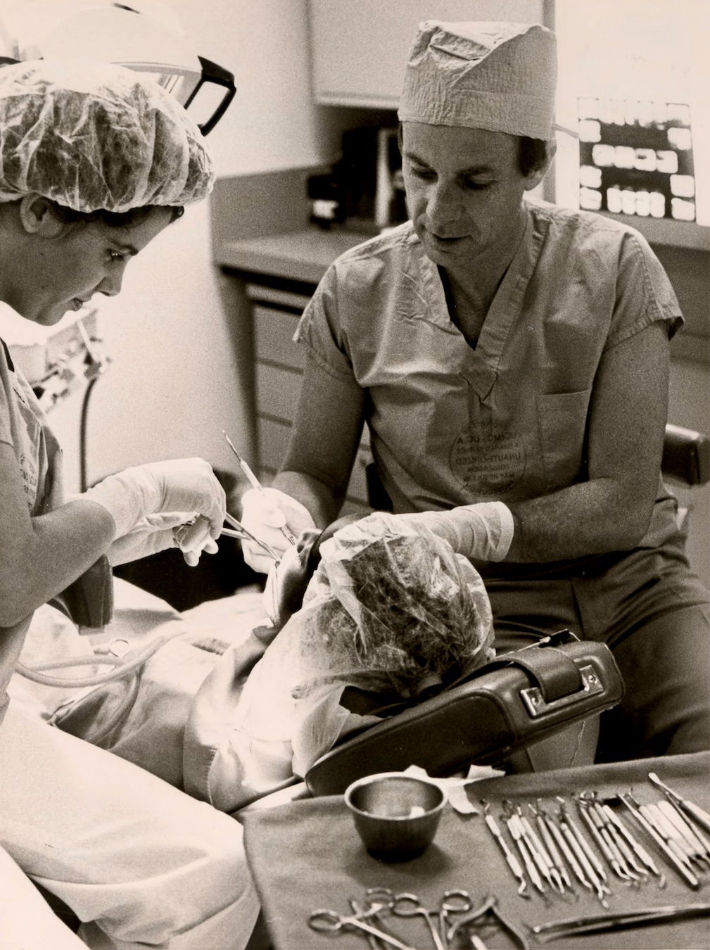 Black-and-white photo of UCLA Dentistry’s Dr. Barrie Kenney and dental technician working on a patient, 1985