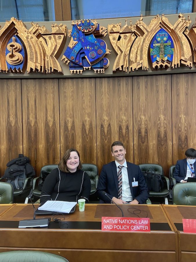 Two UCLA Law students sit at table with Indigenous carvings above