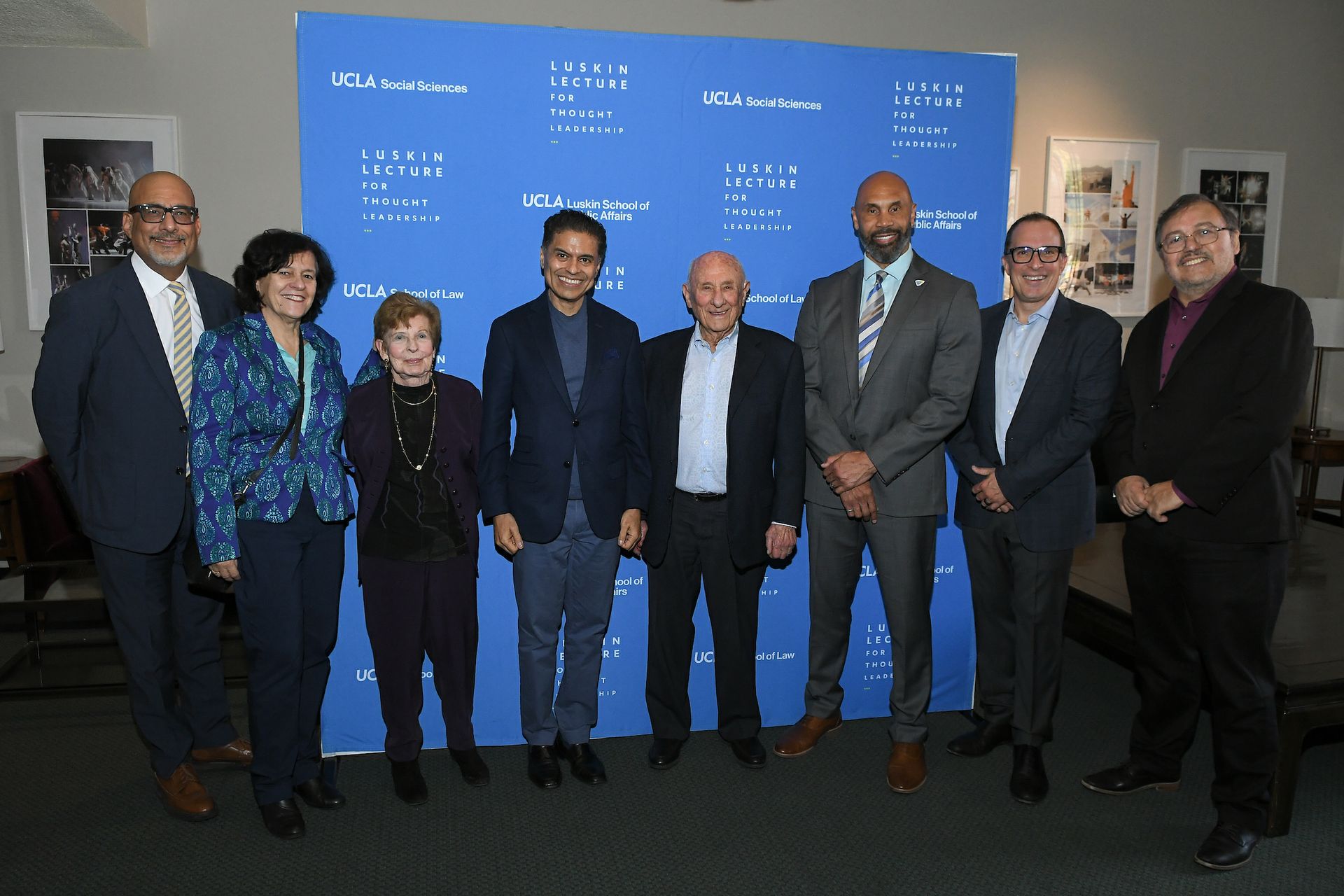 Eight people stand in front of “Luskin Lecture for Thought Leadership” sign