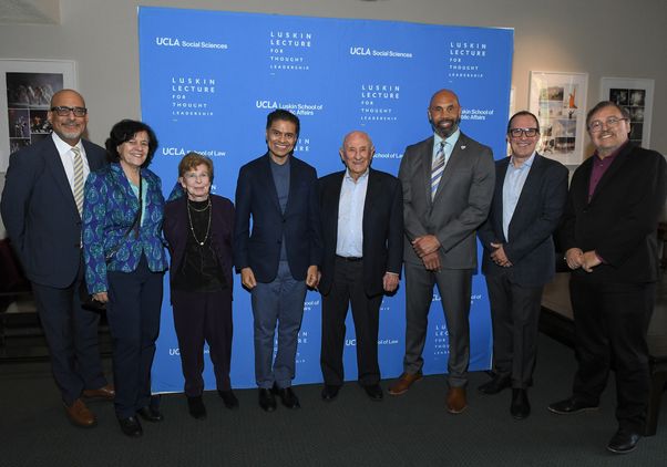 Eight people stand in front of “Luskin Lecture for Thought Leadership” sign