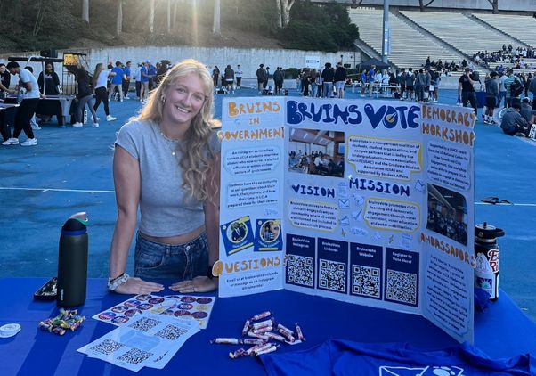 Student standing outside in stadium at table with triptych featuring voting information