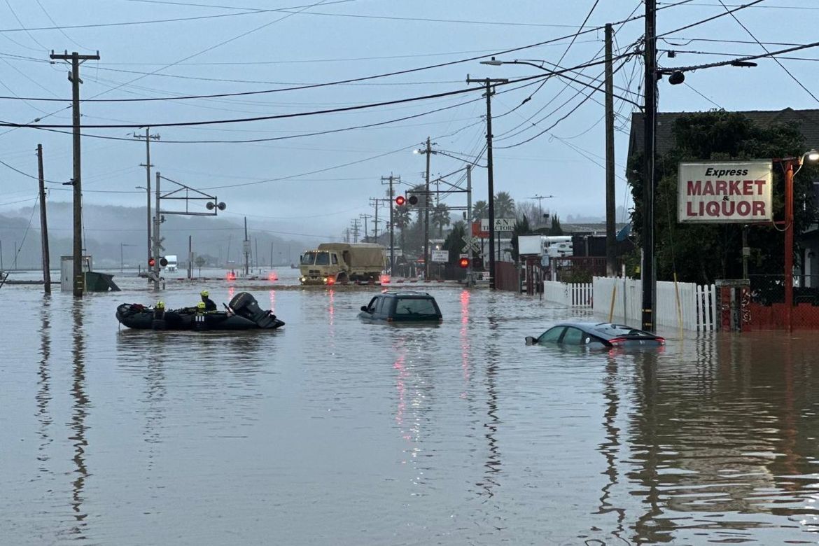 Submerged cars float in the forefront as a National Guard vehicle approaches a flooded railroad track in Monterey County California