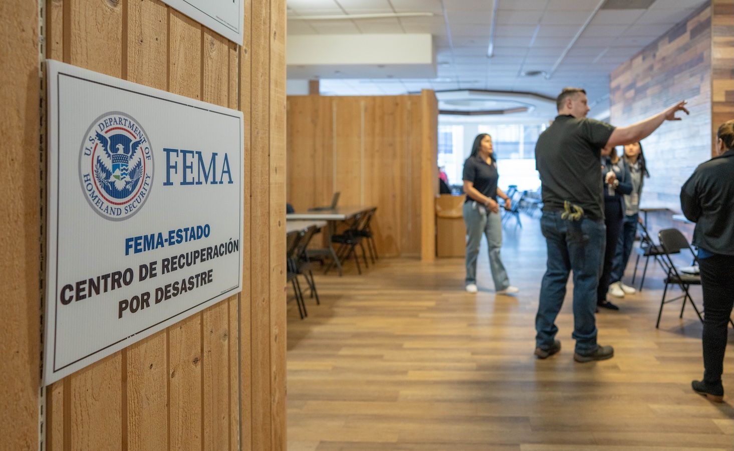 FEMA disaster recovery center sign in Spanish, with support staff in the background
