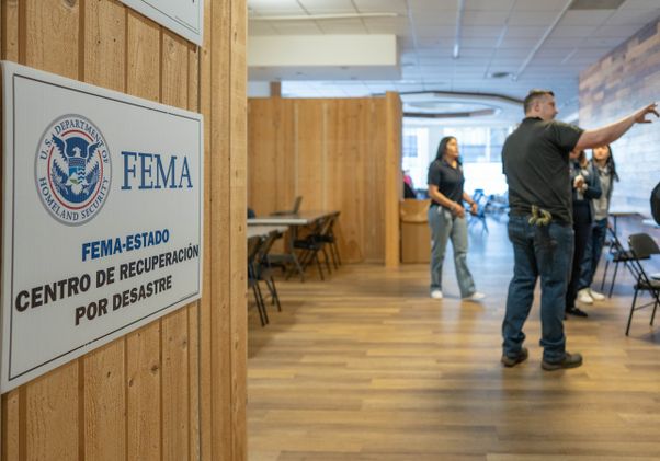 FEMA disaster recovery center sign in Spanish, with support staff in the background