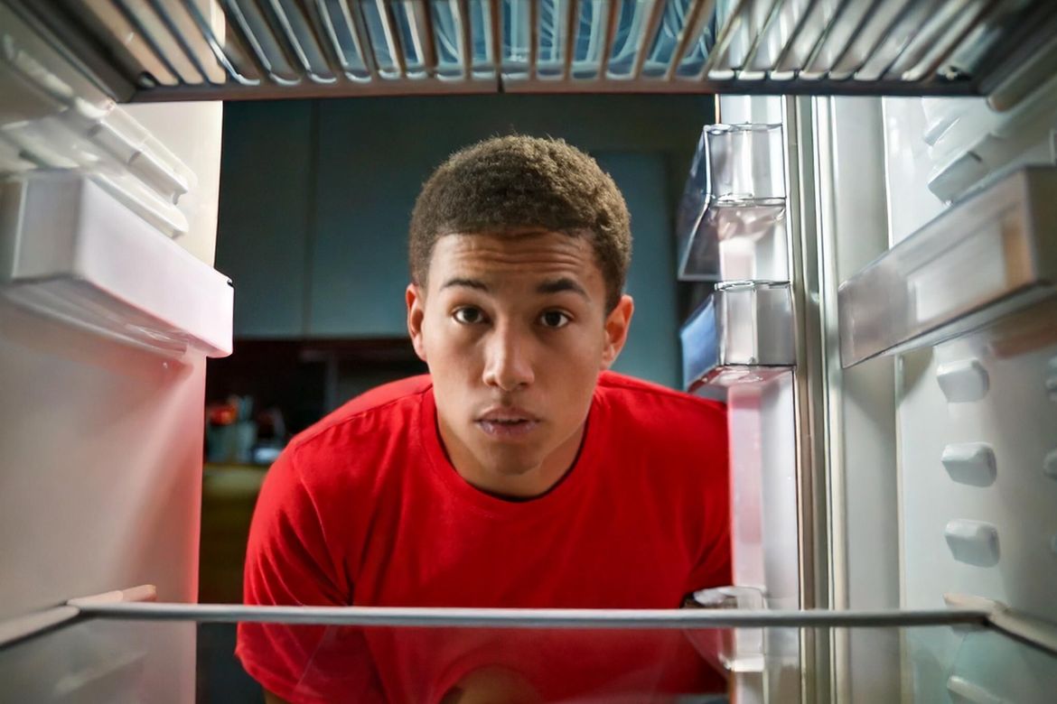 Young Black adult looks into an empty refrigerator