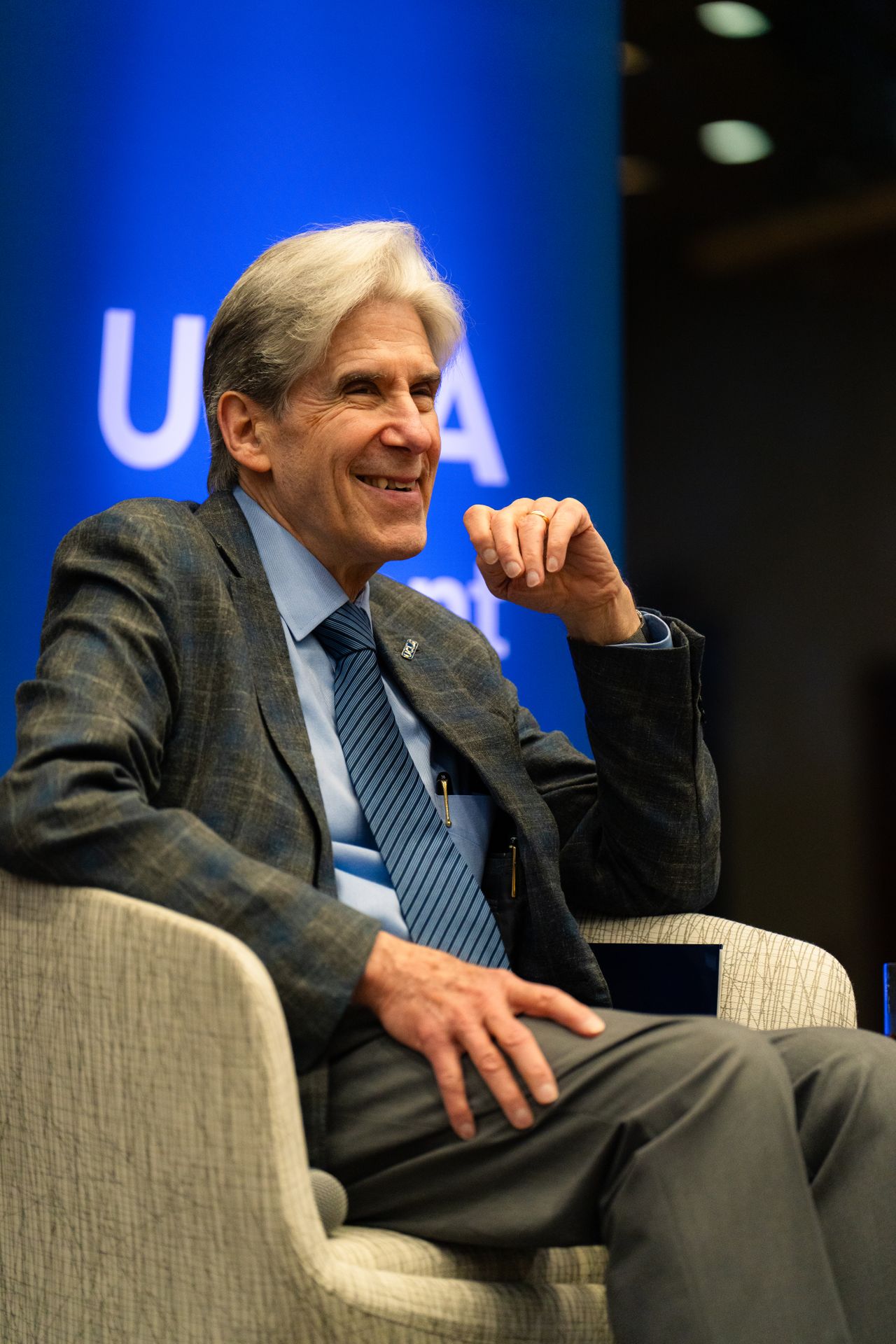 Julio Frenk, in a gray suit, smiles as he sits in a cream-colored chair