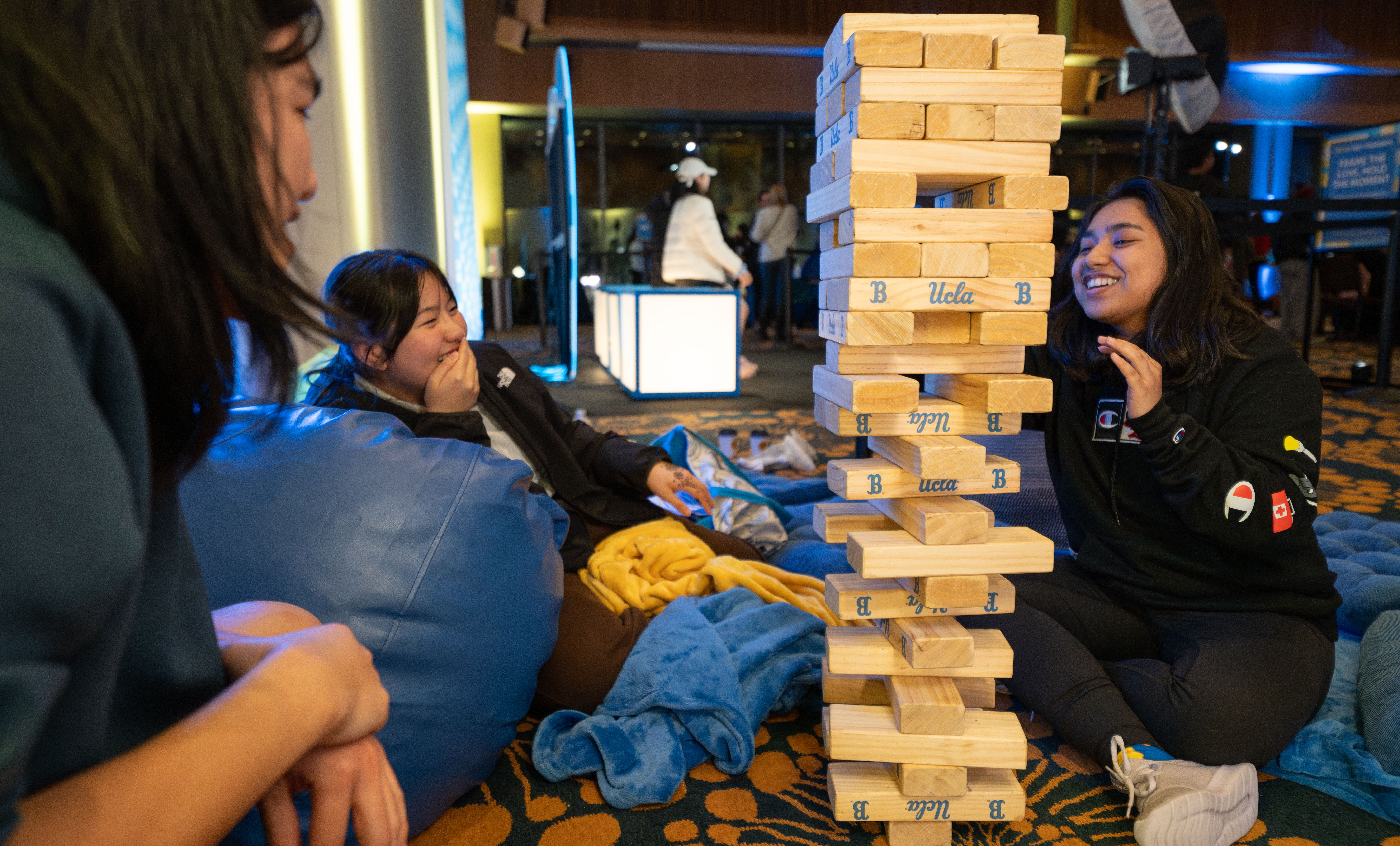 Three students smile as they stack big wooden blocks