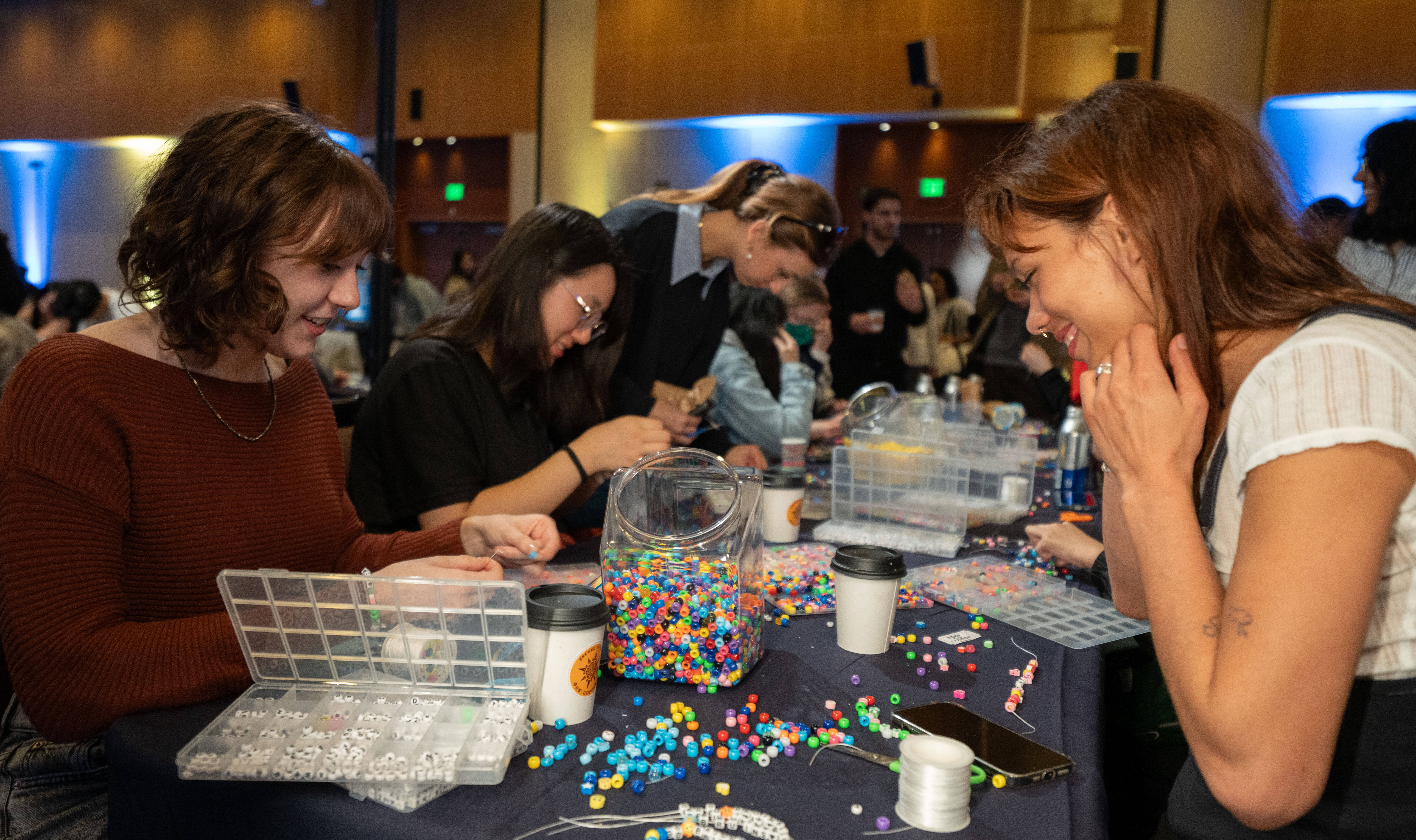 Two students smile as they sit at a table stringing bead bracelets