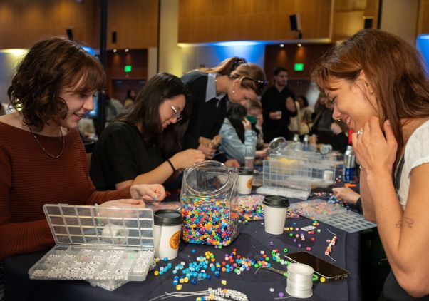 Two students smile as they sit at a table stringing bead bracelets