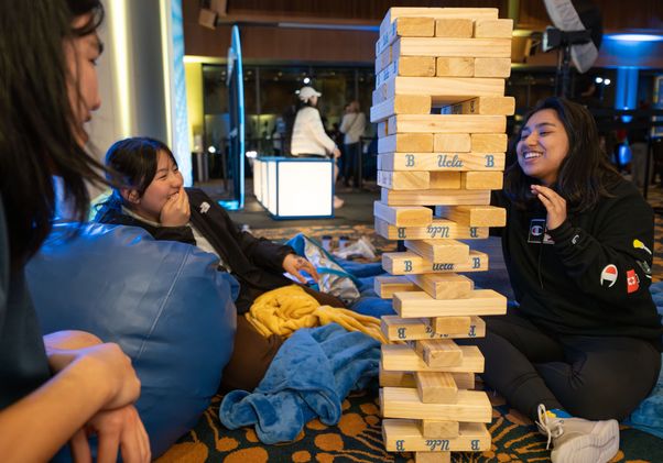 Three students smile as they stack big wooden blocks