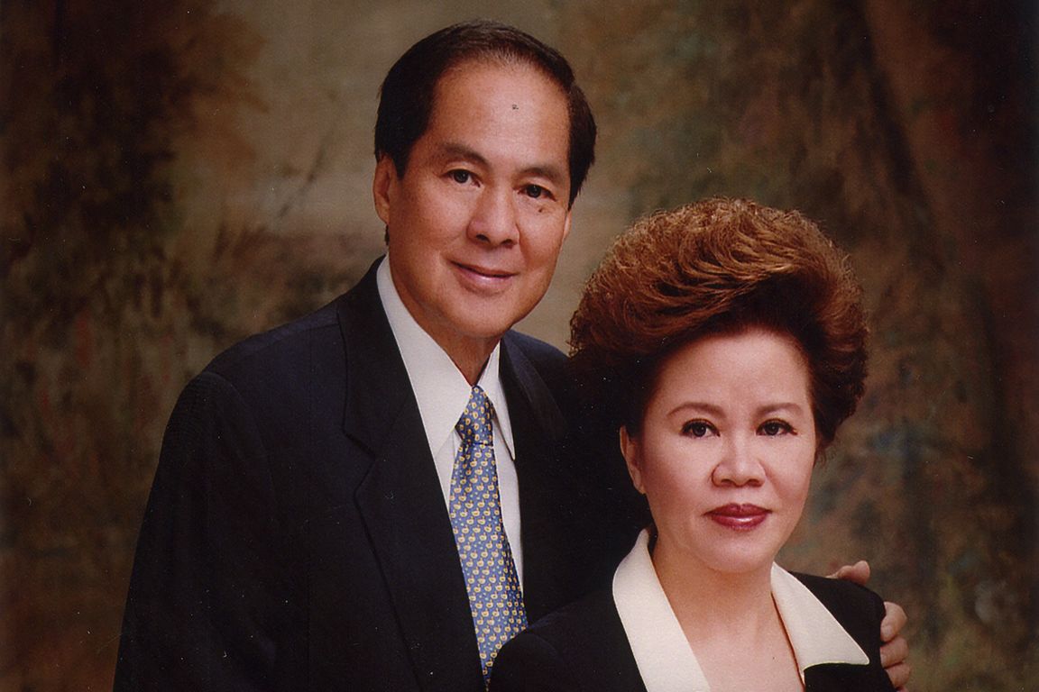 Formal portrait of Karmaka Surjaudaja (left) and Lelarati Lukman standing close together, both dressed in dark business attire, with Surjaudaja wearing a patterned tie and Lukman in a collared blouse, posed against a softly textured studio backdrop