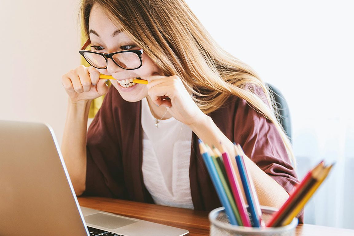Woman biting pencil as she looks at the computer screen