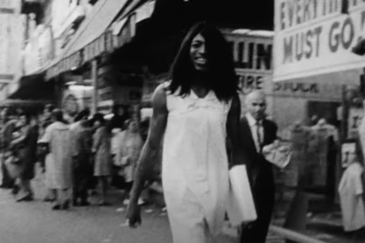 A black-and-white photo of a smiling person walking along a busy street