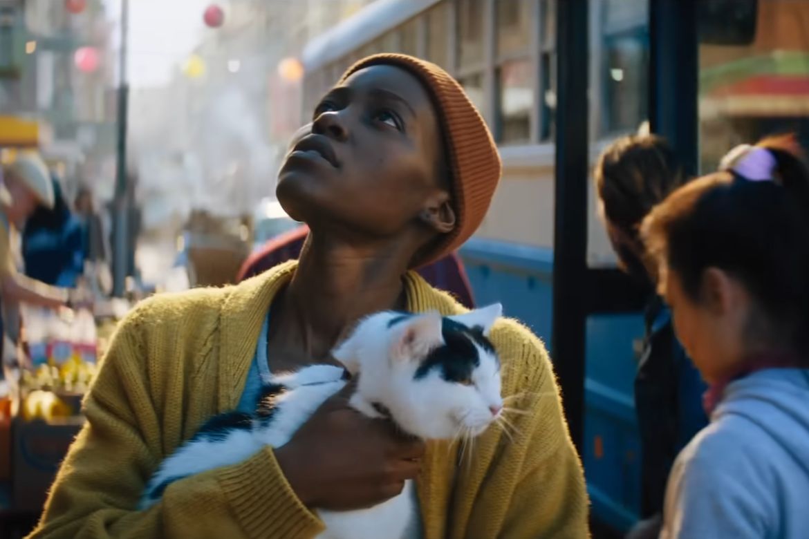 Lupita Nyong'o looks up at the sky, holding a cat, in a scene from “A Quiet Place: Day One.”