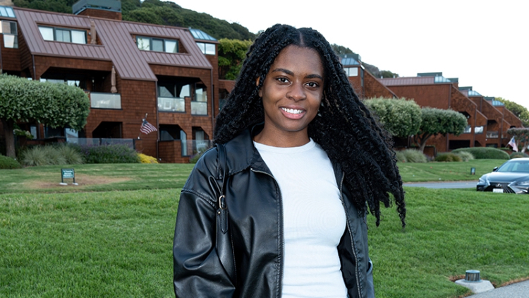 Itohan Ero stands in front of a green lawn and a housing complex