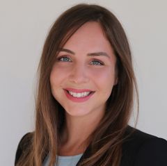 Headshot of Kristen Lee, smiling, with long brown hair, wearing a black blazer over a light blue top, against a neutral background. 