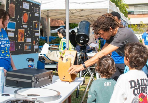Exploring Your Universe 2025: Two kids are shown an experiment next to a telescope