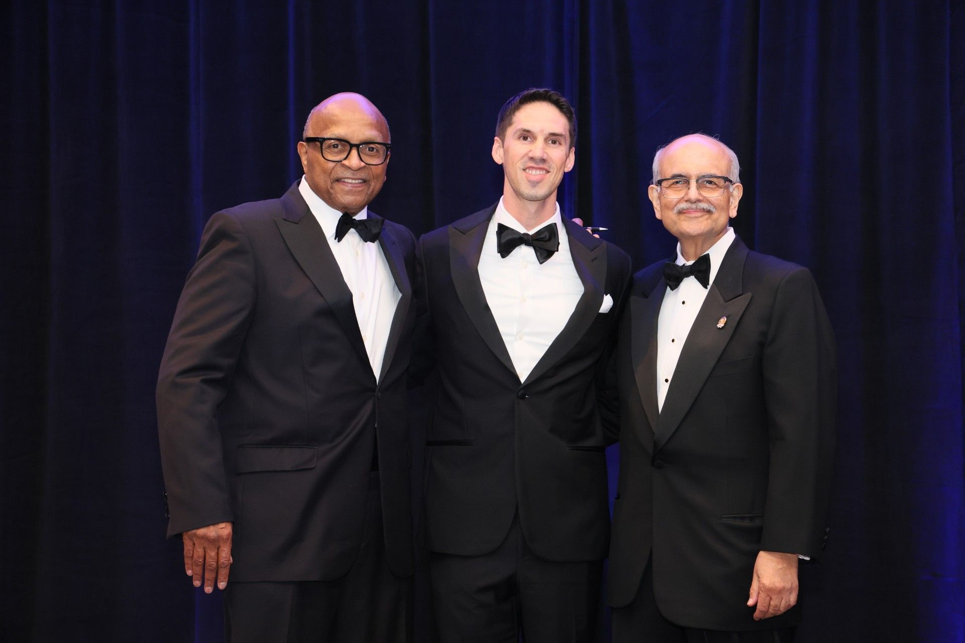 Three men standing together in tuxedo suits; Justin Wagner is in the center