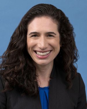 Headshot of Jennifer Sumner smiling, wearing a blue top and dark blazer, against a blue background.