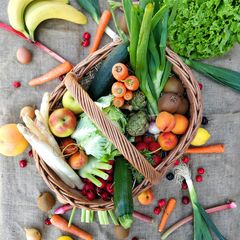 A basket containing colorful fruits and vegetables, including carrots and peaches.