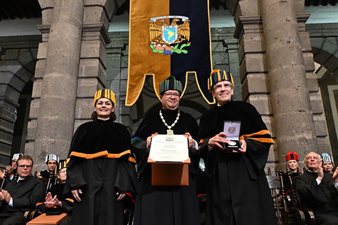 Three people wearing black robes and hats; man in center holds a diploma while Julio Frenk, right, holds up a medal