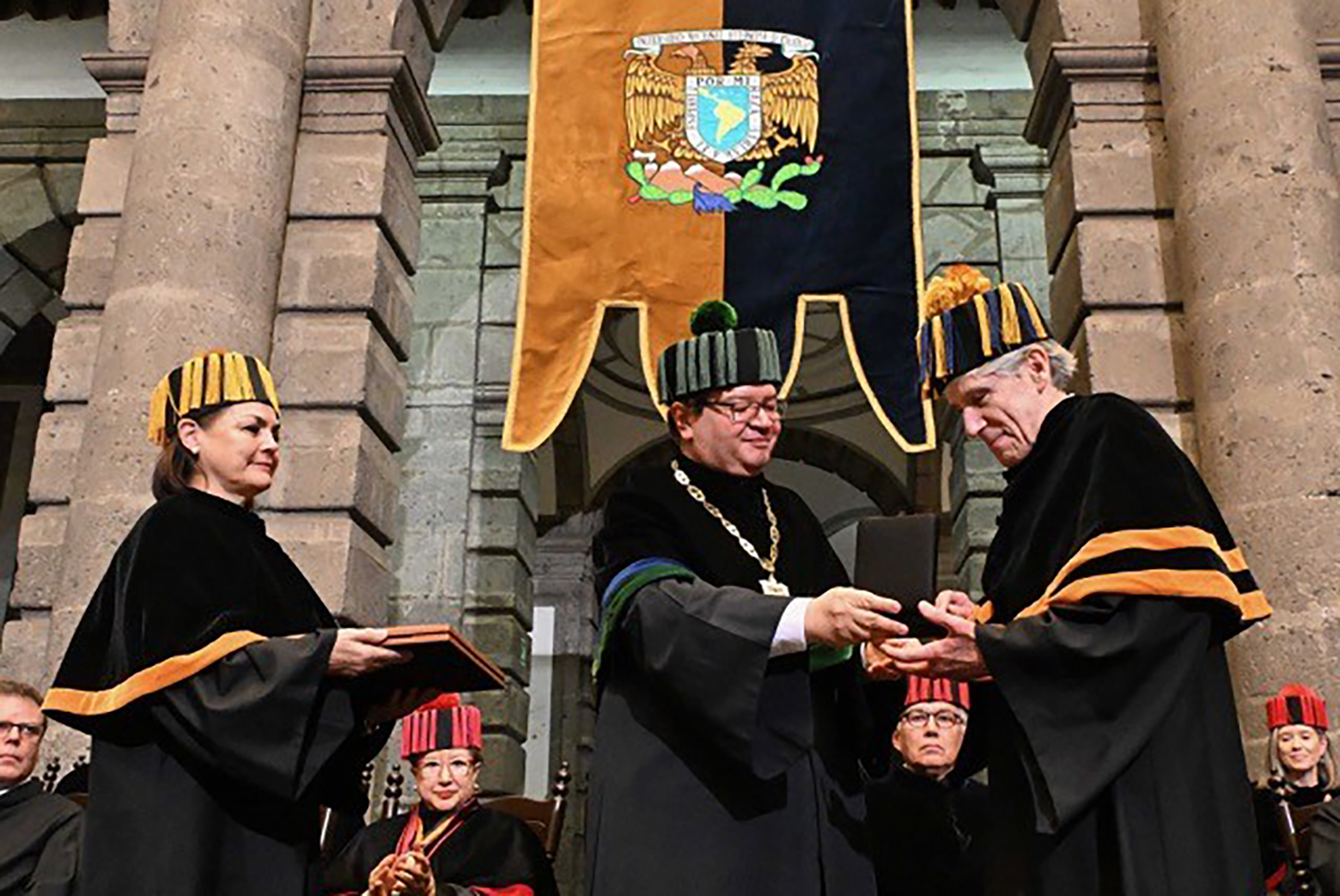 Woman, left, holds diploma covers as man in center presents Julio Frenk with a medal