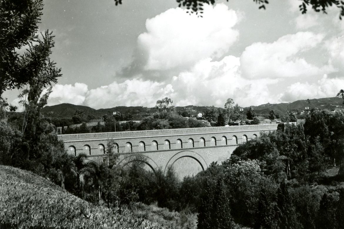 Black-and-white photo of a bridge surrounded by hills and trees