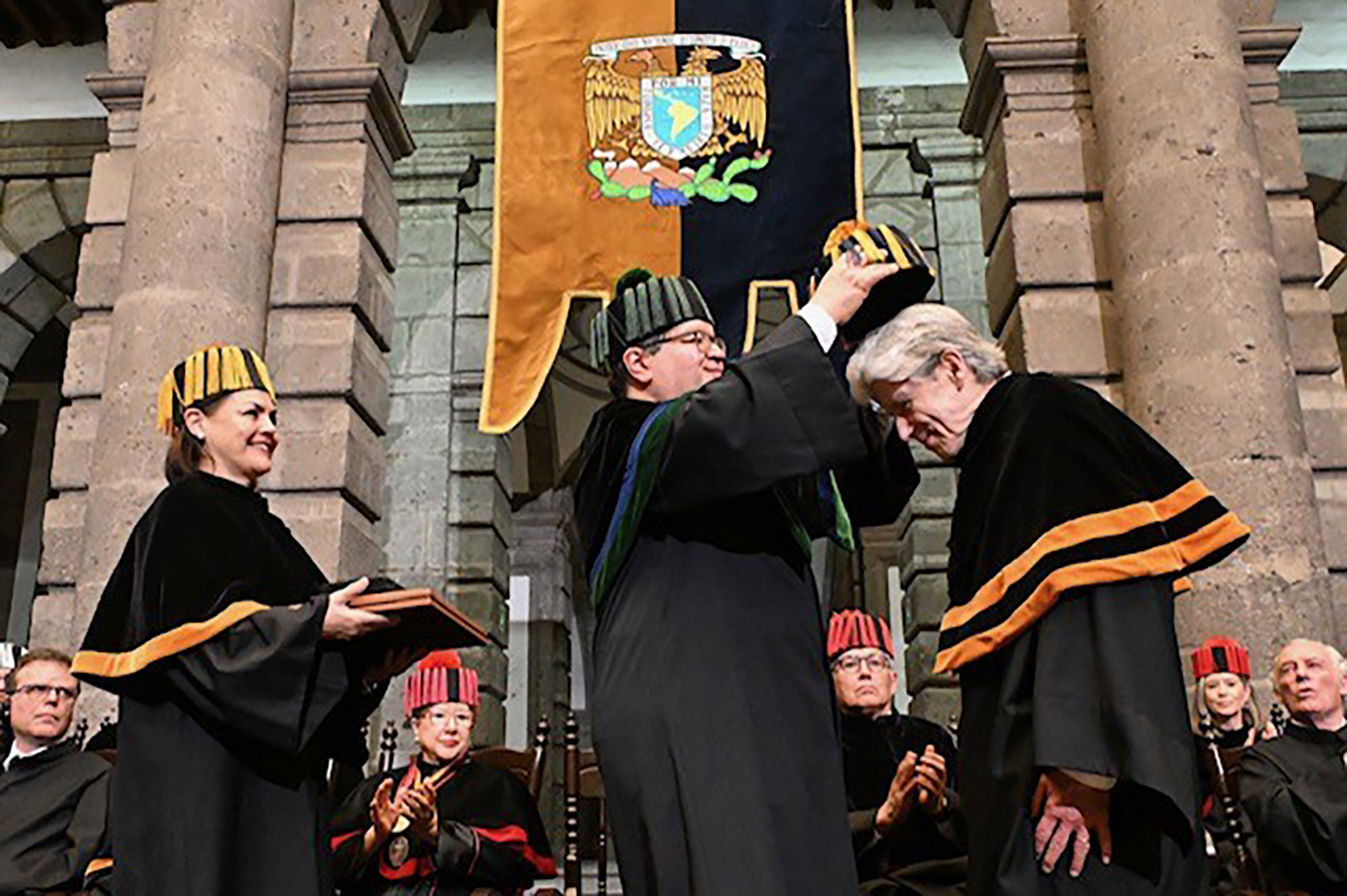 Woman, left, smiles as she watches man in center place a hat on Julio Frenk's head