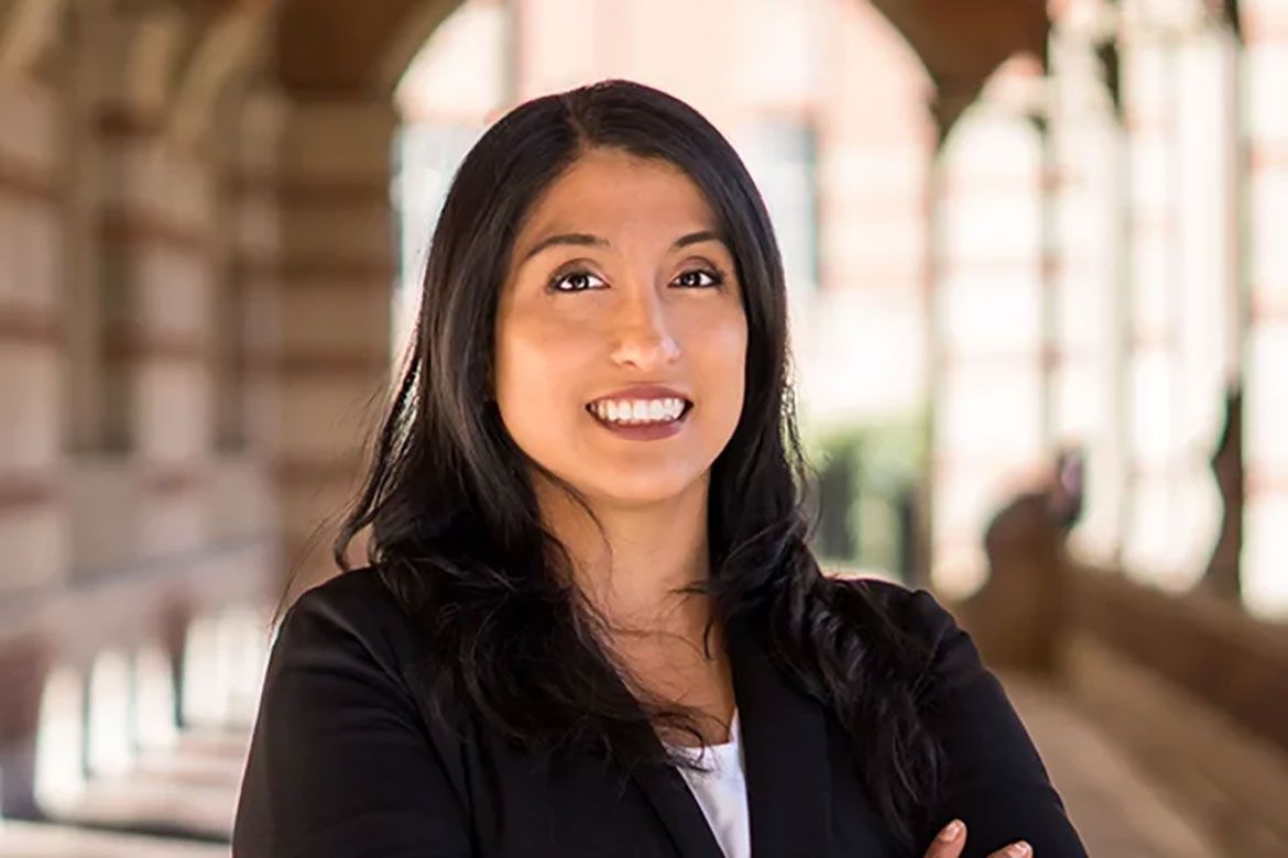 Rosario Jaime-Lara smiles with arms crossed beneath an archway on the UCLA campus.