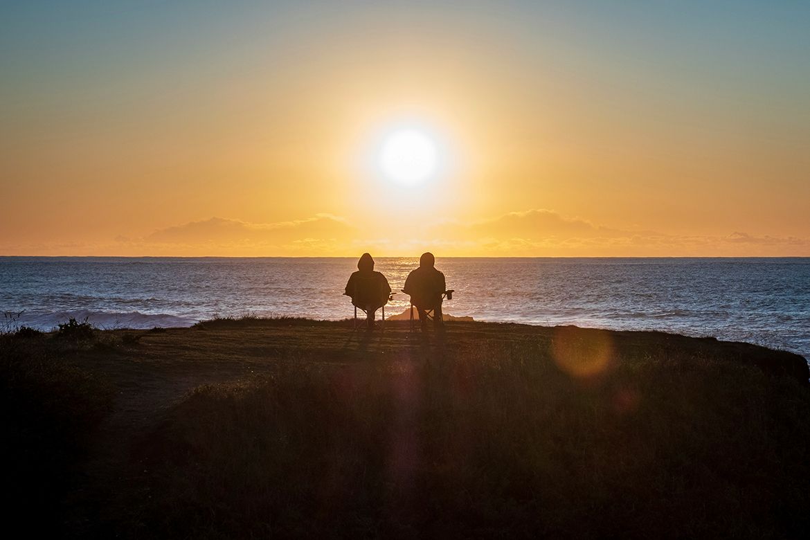 Two people sitting on the seashore watching the sunset