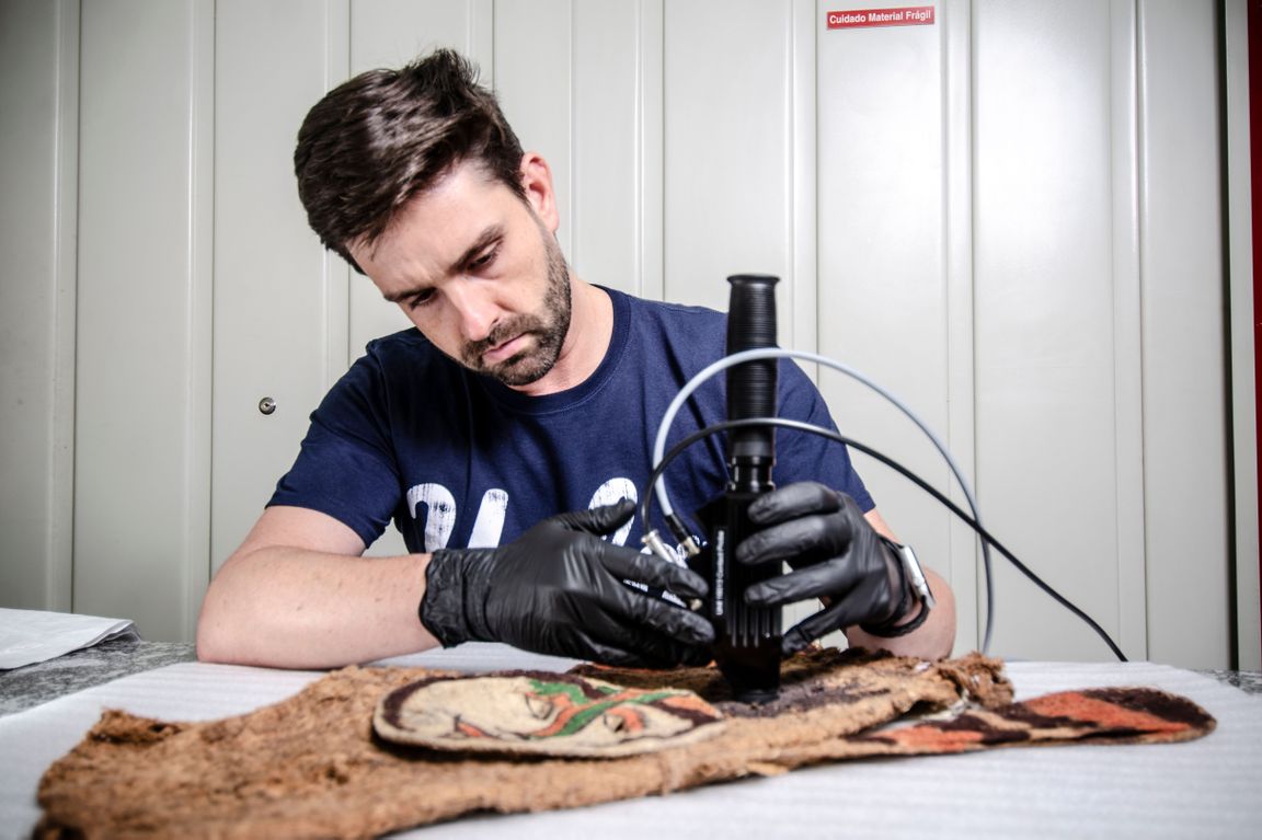 Man in blue shirt and black gloves holding device over an artifact