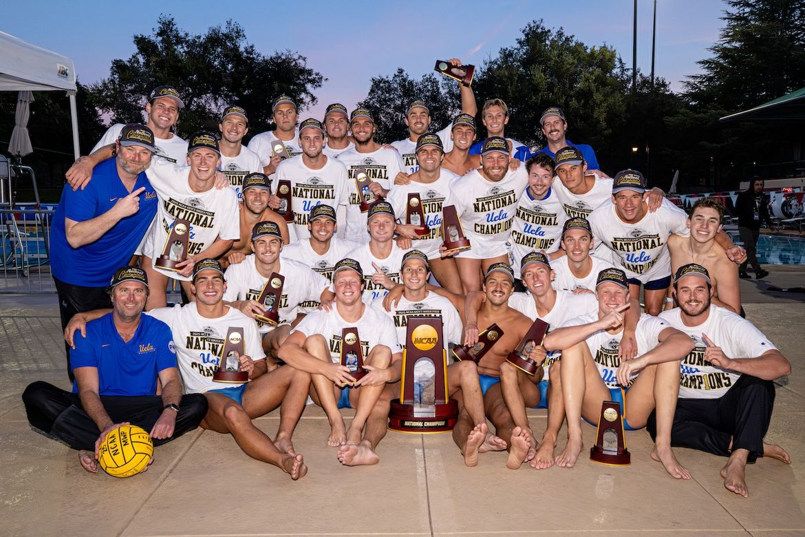The UCLA men's water polo team and coaches pose poolside with the NCAA National Championship trophy and individual awards, wearing "UCLA National Champions" shirts and hats.