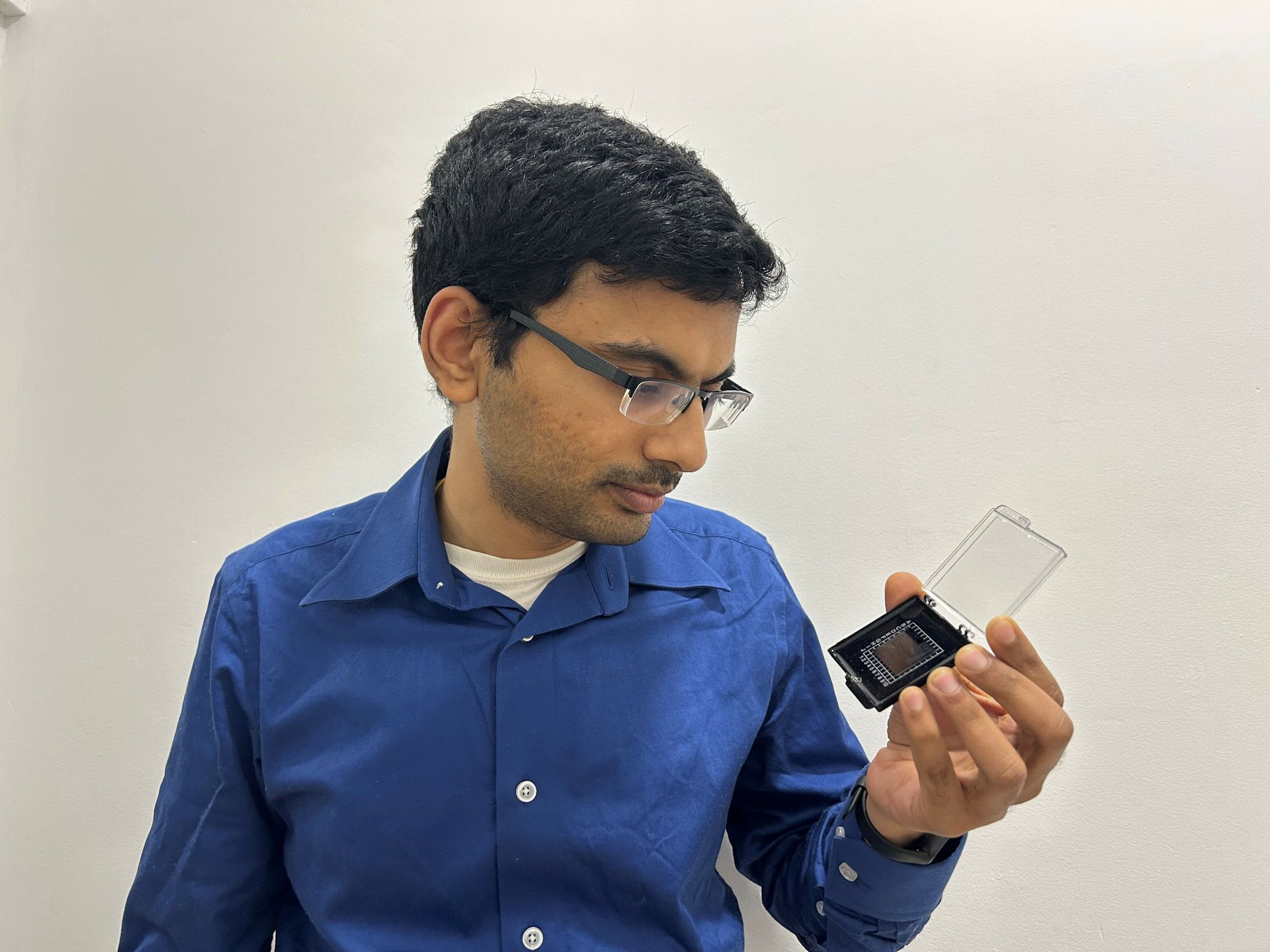 Pradip Gatkine, in blue button-down and glasses, holds a photonic chip in left hand