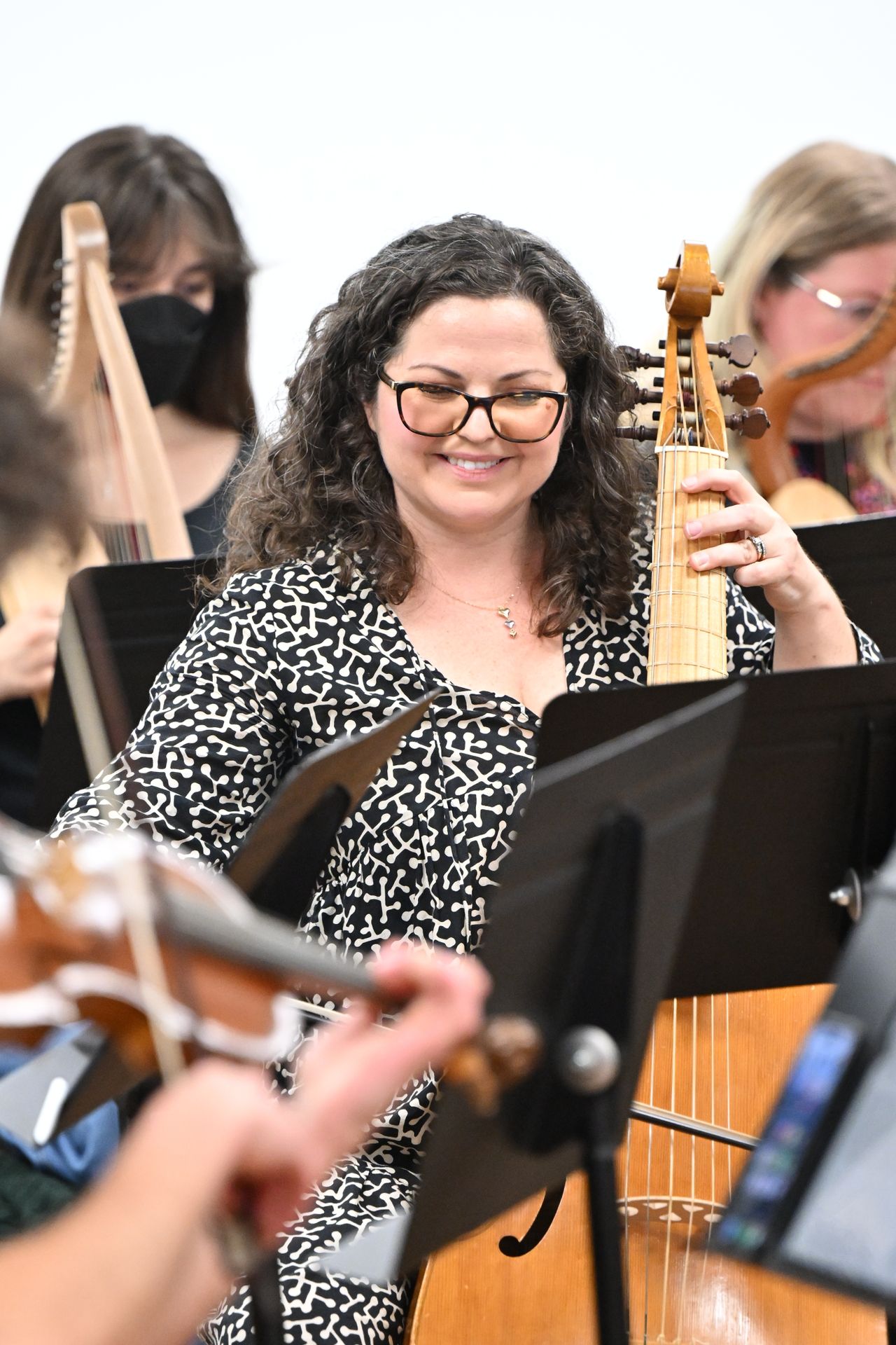 Marylin Winkle, in black patterned dress and glasses, smiles as she plays a viola da gamba