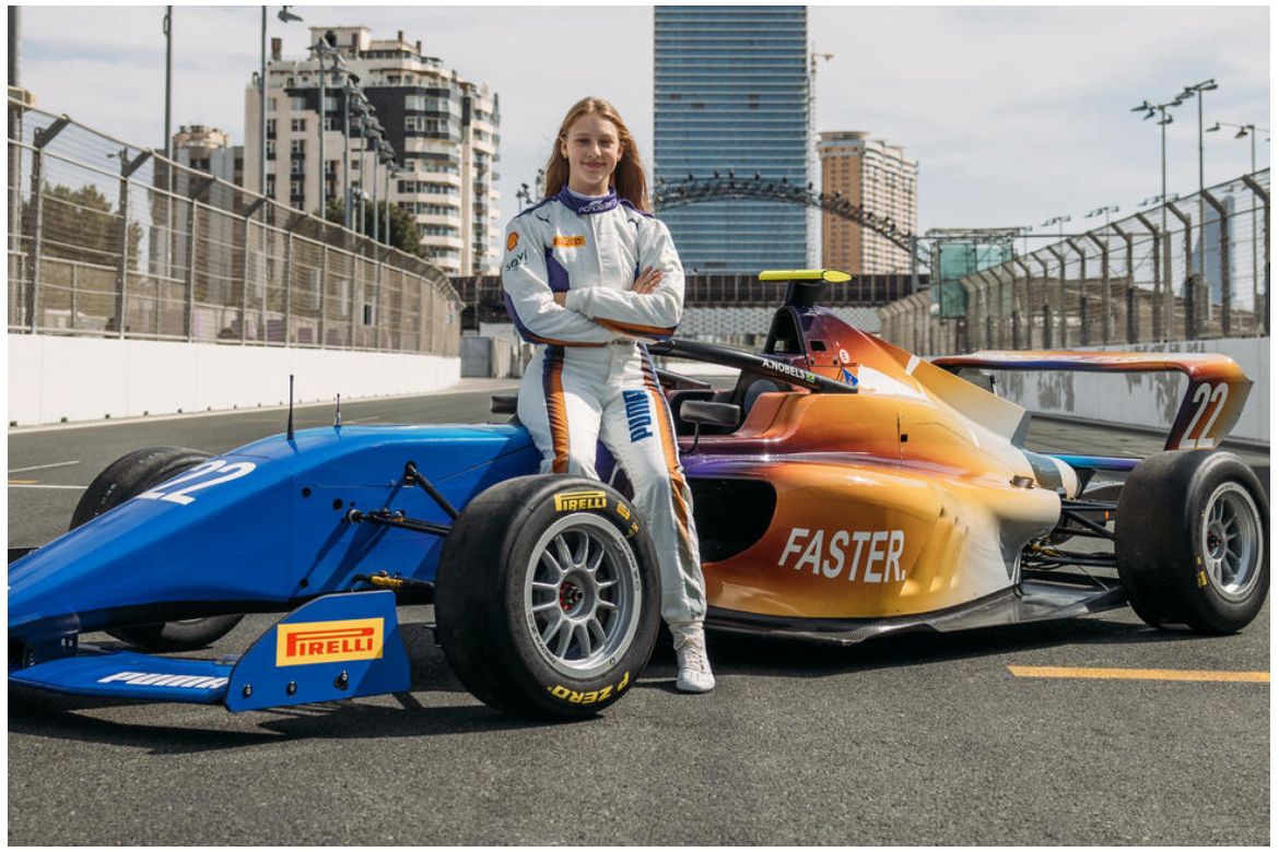 Auriela Nobels stands in front of a blue-and-orange liveried open-wheel race car