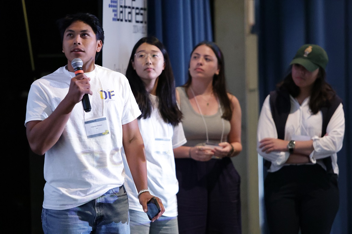 Four students, far left holding a microphone, onstage at DataFest