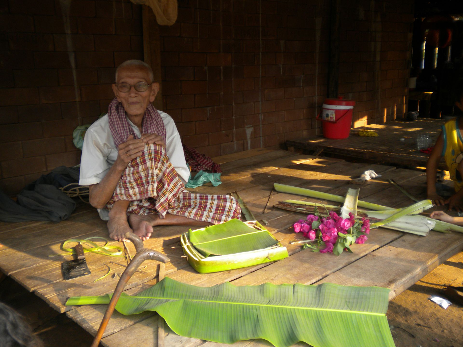 Cambodian man surrounded by large bright green leaves and pink flowers